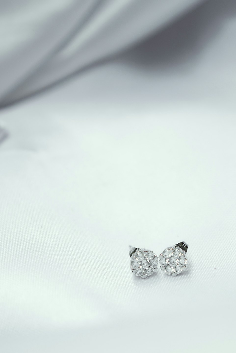 Deux boucles d'oreilles argentées en grappe posées sur un tissu blanc.