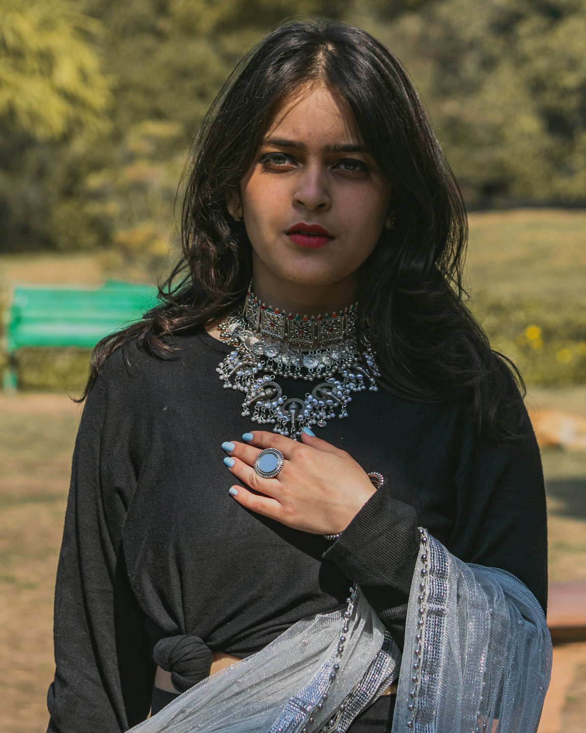 Une femme portant d'intricats bijoux en argent se tient dans un parc.