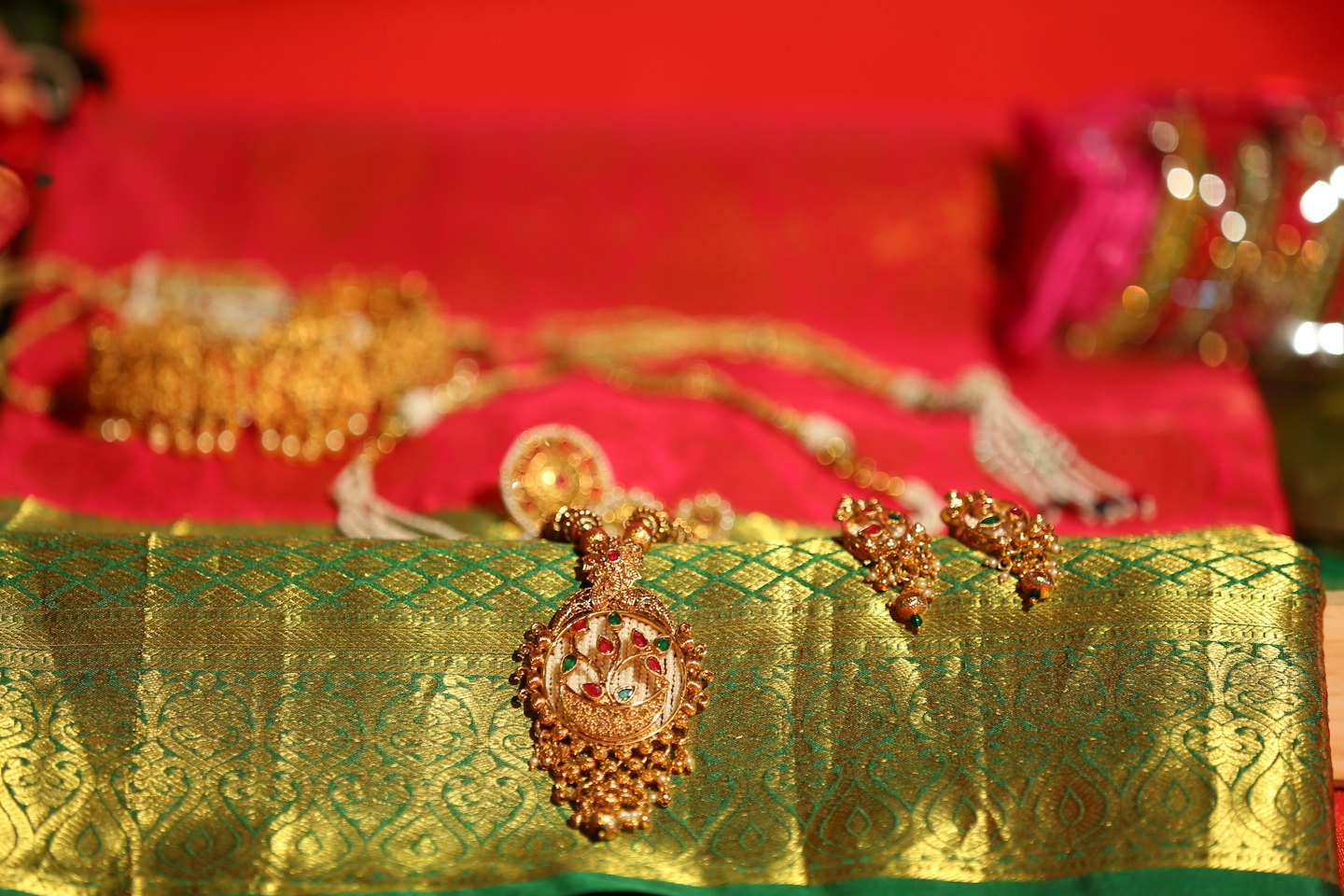 Pendentif et boucles d'oreilles complexes en or posés sur un tissu de soie à motifs.
